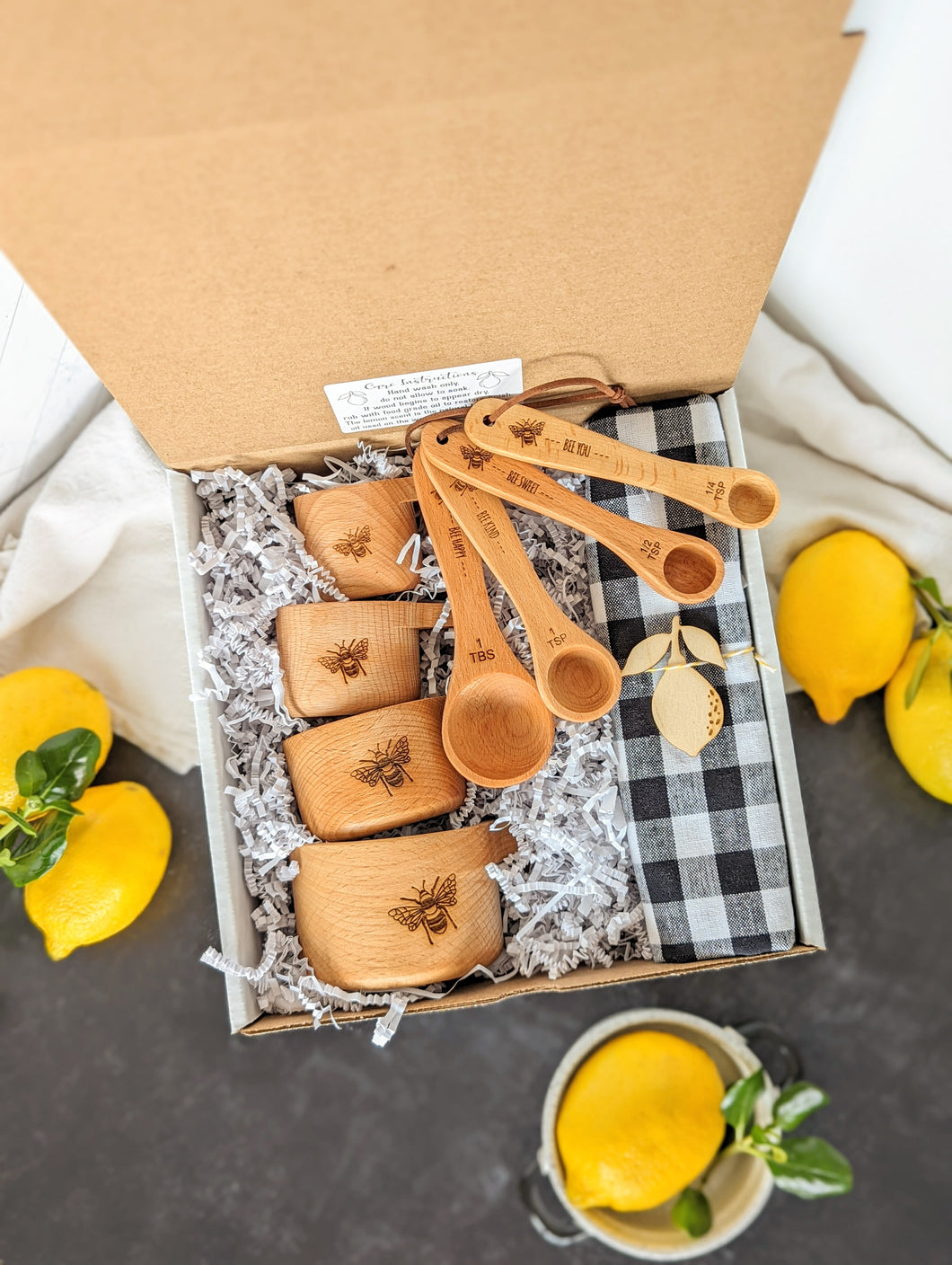 gift box containing- measuring cups, measuring spoons, dishtowel, and lemon shaped wooden magnet 